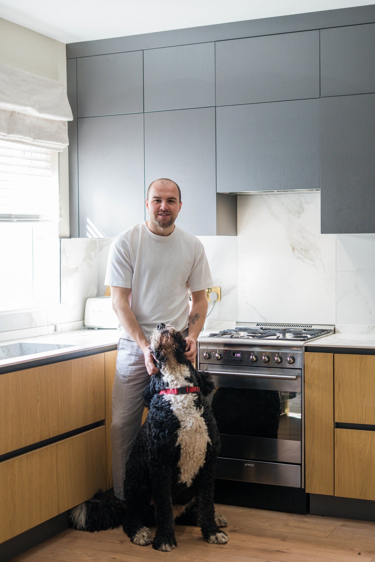 Man and dog standing in a modern kitchen with gray and wooden cabinets. lumantea interiors